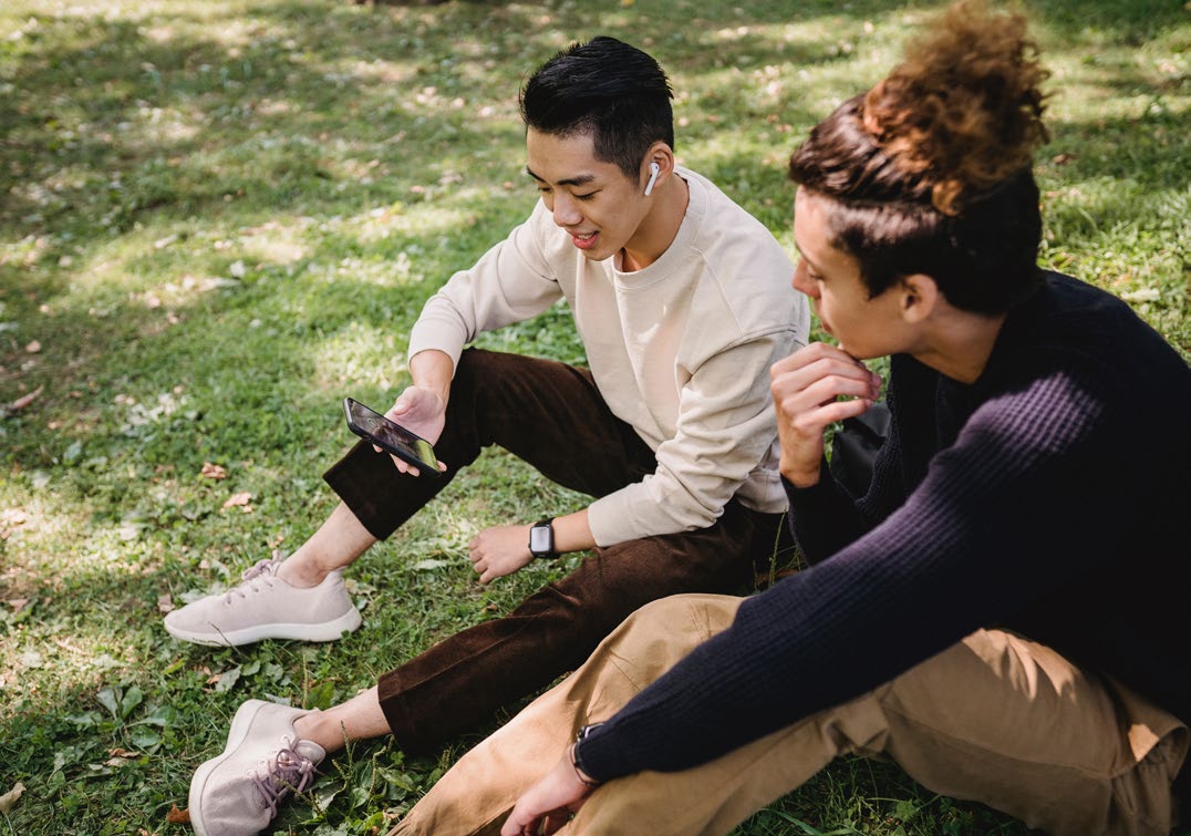 Two people sitting together on the ground looking at a phone.